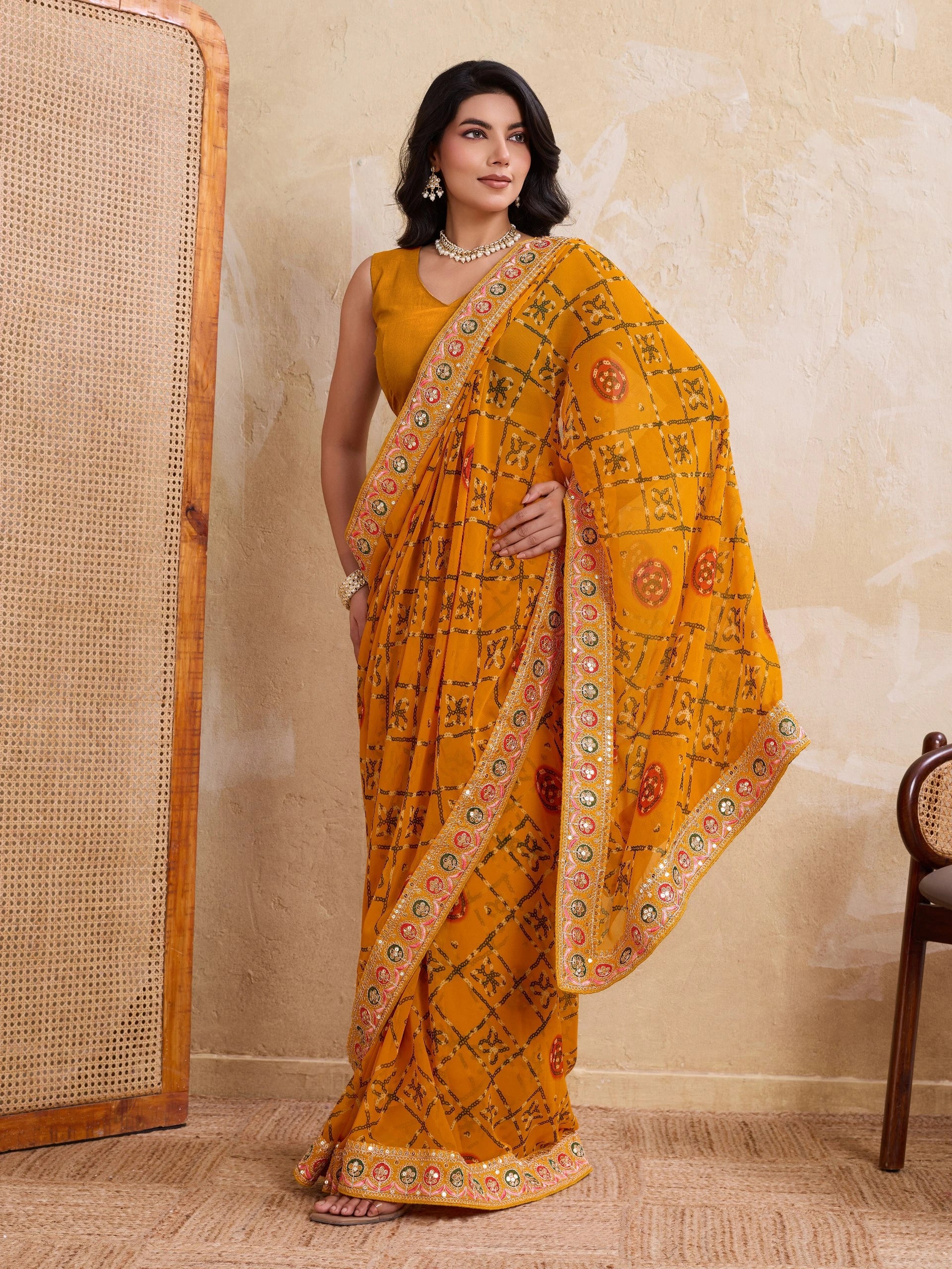 Woman wearing a yellow saree with a floral pattern against a beige wall.